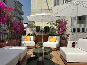 Un espace extérieur aménagé avec des canapés blancs, des coussins jaunes et une table en verre.