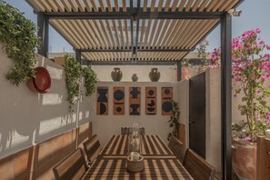 Eine Terrassenausstattung im Freien mit Holztisch und Bänken, umgeben von Blumentöpfen und Dekovasen.