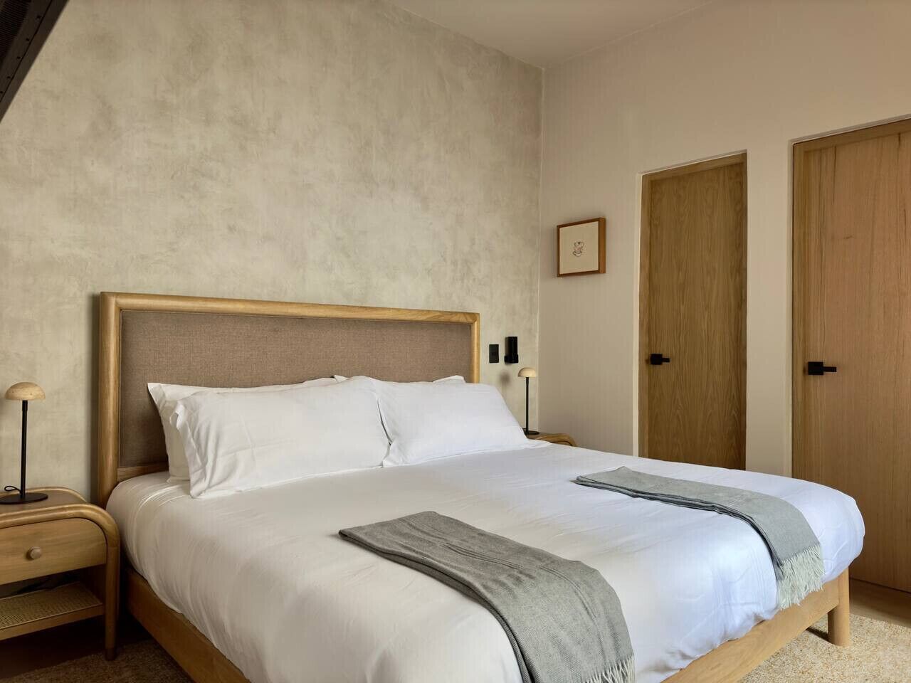 Une chambre à coucher comprenant un lit, deux tables de chevet, une commode, une lampe et deux portes.