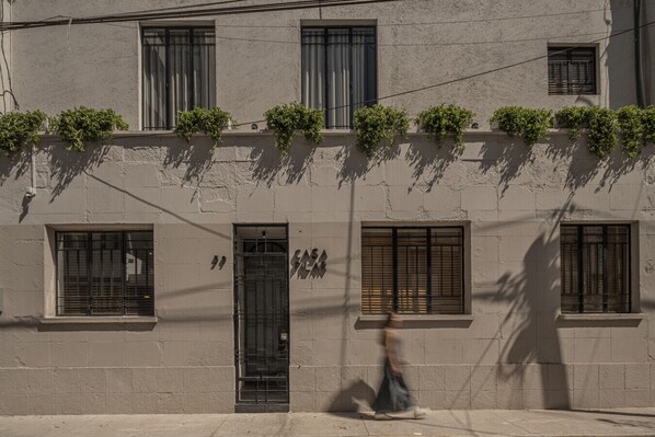 Une façade d’immeuble avec de nombreuses fenêtres, dont certaines sont dotées de volets, et une porte surmontée d’un portail en métal.