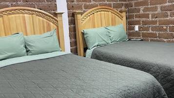 Habitación con dos camas, cada una con cabecero de madera y ropa de cama verde. Las paredes son de ladrillo visto.