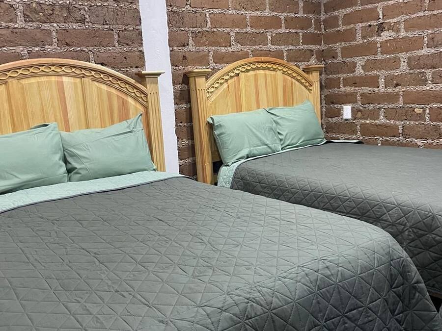 Une chambre avec deux lits, chacun doté d’une tête de lit en bois et d’une literie verte. Les murs sont en briques apparentes.
