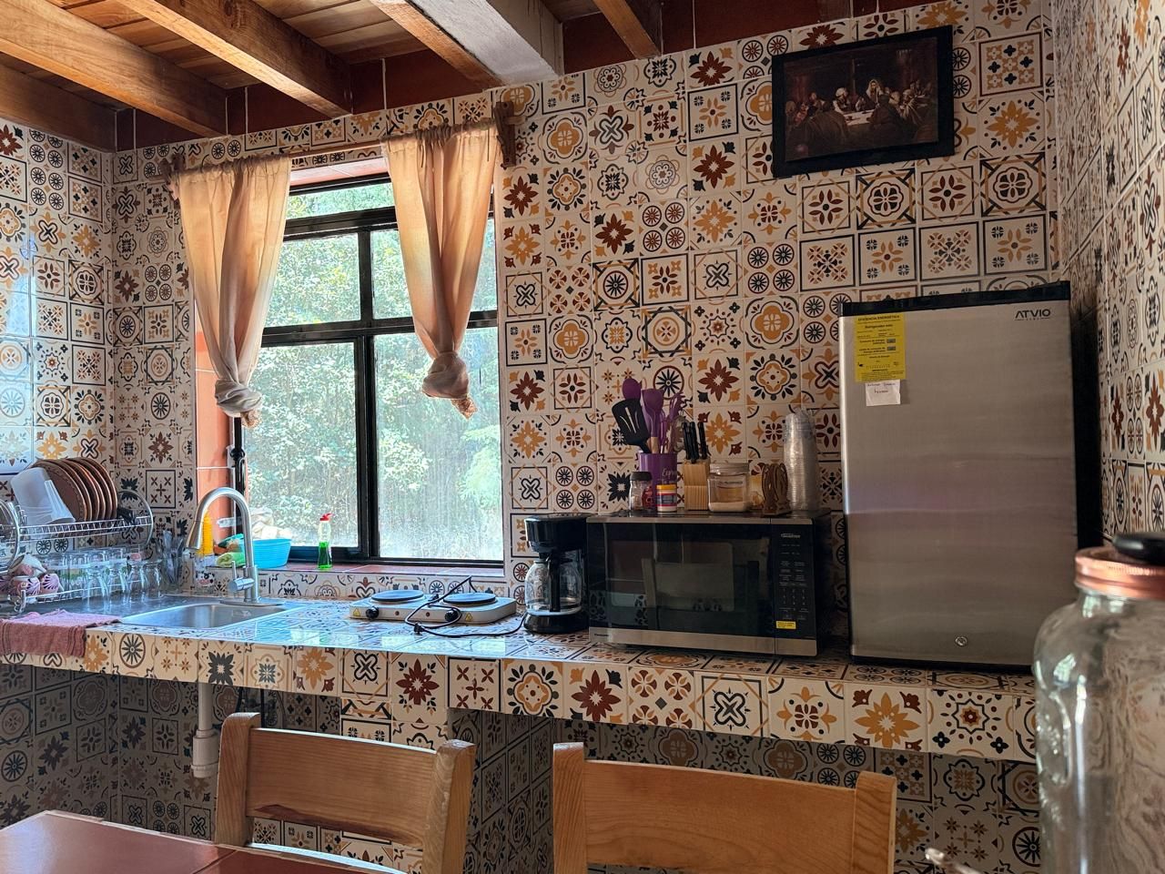 Una cocina con baldosas estampadas, un refrigerador, un microondas y un ventanal con cortinas.