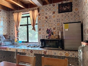 Una cucina con piastrelle decorative, un frigorifero, un forno a microonde e una finestra con tende.