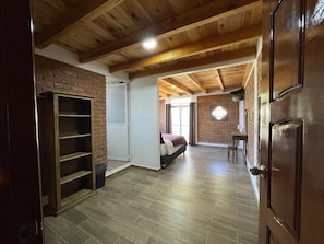 A spacious room with a brick wall, wooden flooring, a bed, a desk, and a shelving unit.