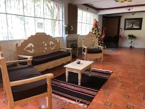 A room with a wooden sofa, a matching armchair, a small table, and a colorful striped rug.