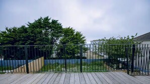 Una terraza de madera con cerramiento metálico, árboles y un edificio al fondo.