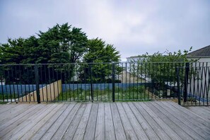 Eine Holzterrasse mit einem Metallzaun, Bäumen und einem Gebäude im Hintergrund.