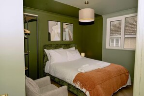 Ein Schlafzimmer mit einem Bett, einem Sessel, einem Nachttisch, einer Lampe und einem Fenster.