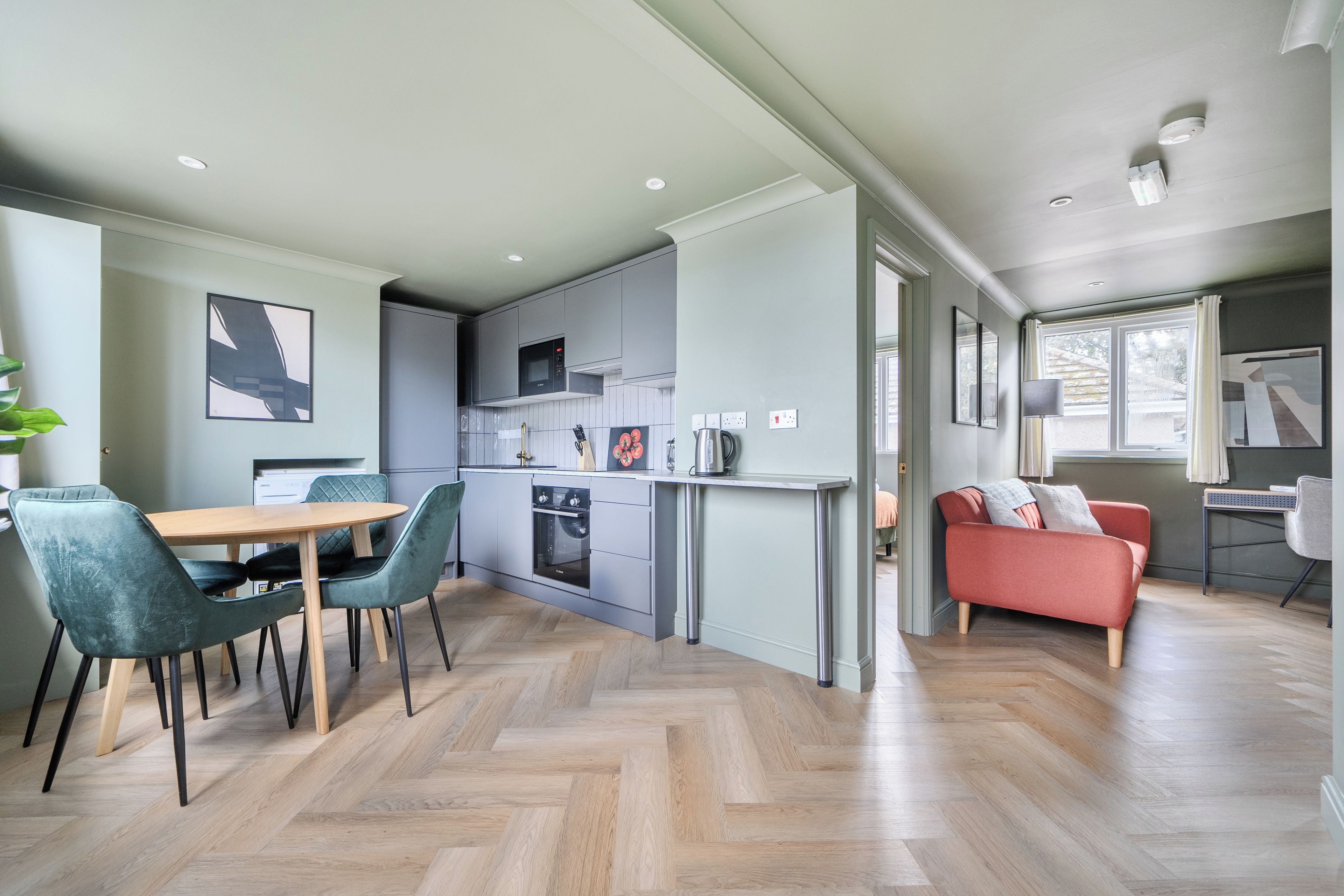 Eine moderne Küche mit Backofen und Mikrowelle, ein Essbereich mit Holztisch und Stühlen sowie ein Wohnbereich mit Sofa und Fenster.