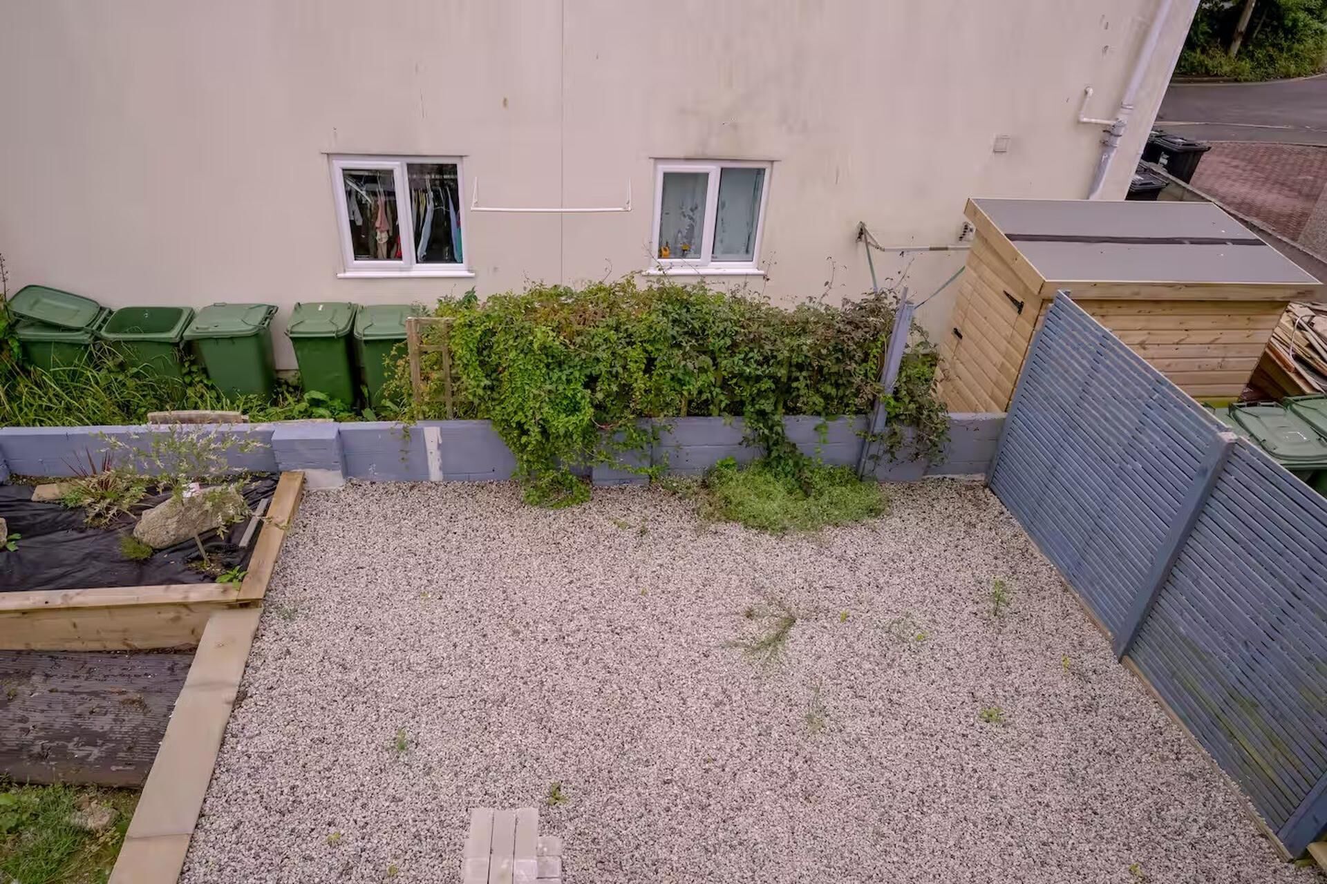 Ein Wohngarten mit Kiesfläche, einem erhöhten Holzkastenbeet und einem Holzzaun.
