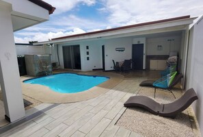 Ein Pool mit Fliesen, eine Liege und ein Küchenbereich mit Schränken und Spüle.