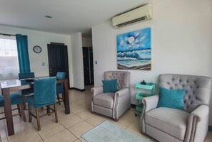 Ein Wohnzimmer mit Esstisch, zwei Sesseln, einem Gemälde und einer Klimaanlage.