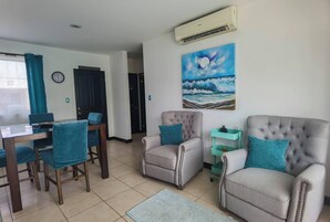 Una sala de estar con una mesa de comedor, dos sillones, un cuadro y un equipo de aire acondicionado.