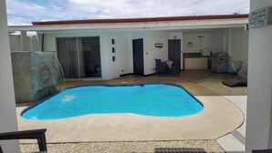Una piscina de borde curvo, un área exterior techada con cocina y un letrero con un mensaje.