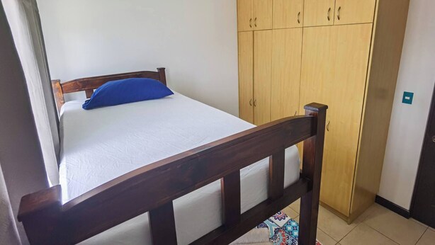 Una cama individual con cabecera de madera, un almohadón azul y un armario de madera.