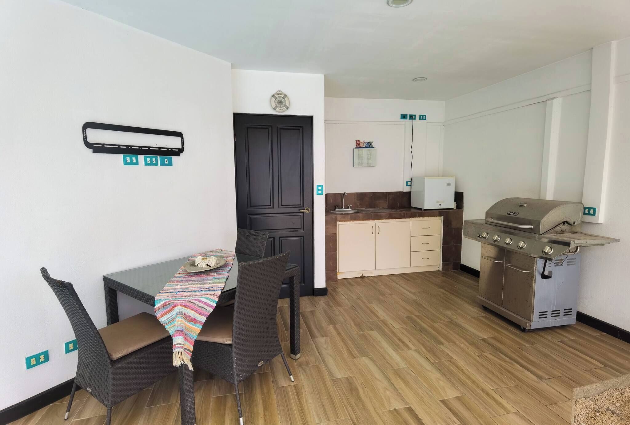 Une cuisine compacte dotée d’un barbecue intégré, d’un coin repas avec une table et des chaises, et d’une porte affichant un panneau de sécurité incendie.
