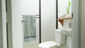Un baño con inodoro, toallero, lavamanos y estante con una planta.