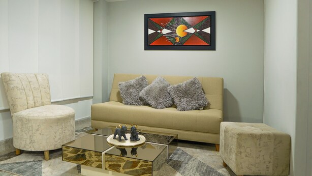 Una sala de estar con un sofá color beige, dos sillones, una mesa de centro con figuritas y un cuadro abstracto moderno en la pared.