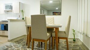 Un comedor con una mesa y cuatro sillas, una cocina con microondas y un espejo en la pared.