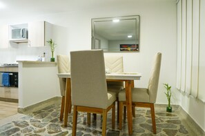A dining area with a table and four chairs, a kitchen with a microwave, and a mirror on the wall. - Heart of Laureles: Beautiful 2BR Near Best Cafes & Restaurants (Antioquia)