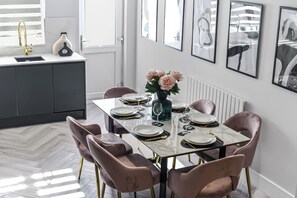 Ein Essbereich mit einem Marmortisch, gedeckt für sechs Personen, umgeben von rosa Stühlen mit goldfarbenen Beinen.