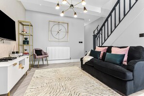 Ein modernes Wohnzimmer mit einem schwarzen Sofa, einer weißen TV-Konsole, einem Bücherregal mit goldener Rahmung und einer großen Wanduhr.