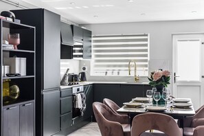 A modern kitchen with black cabinetry, a built-in oven, and a dining area with a table set for four. - The Ultimate Hangout 4BR Modern House with Garden (Enfield)