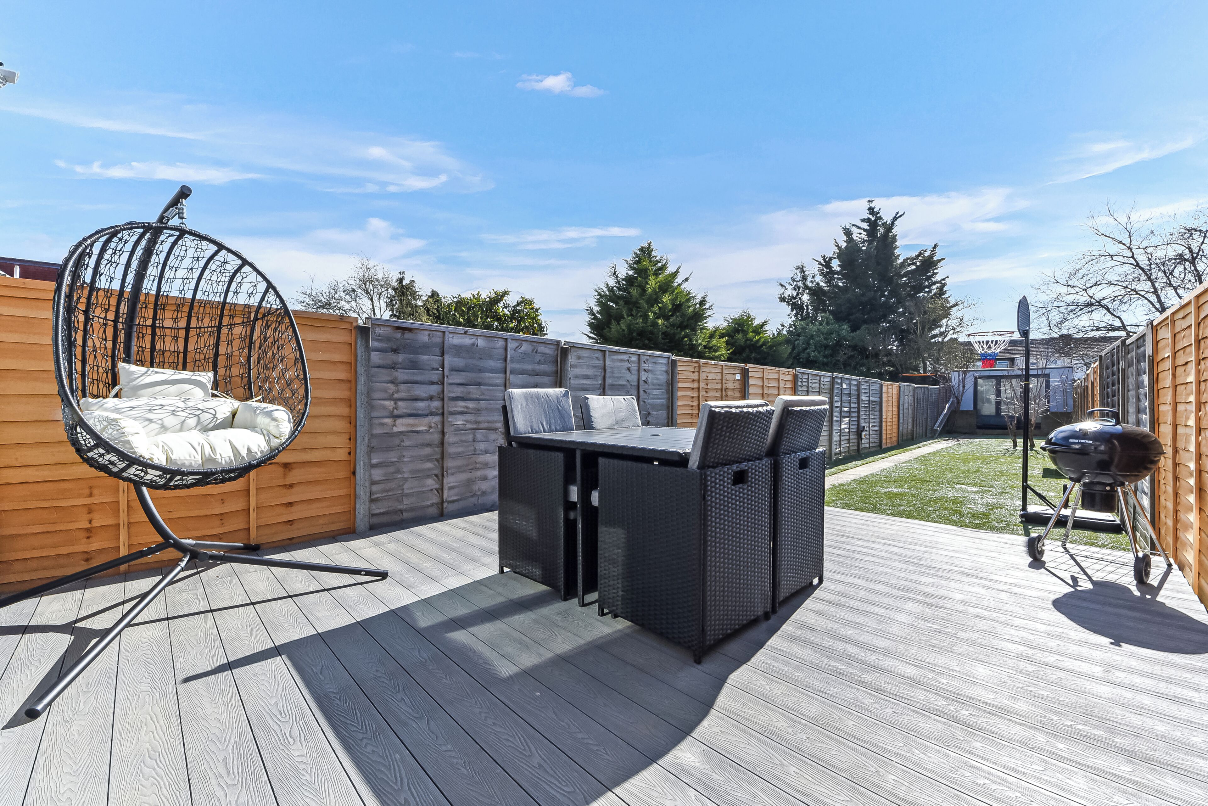 A patio with a hanging chair, a grill, and a table with cushions.