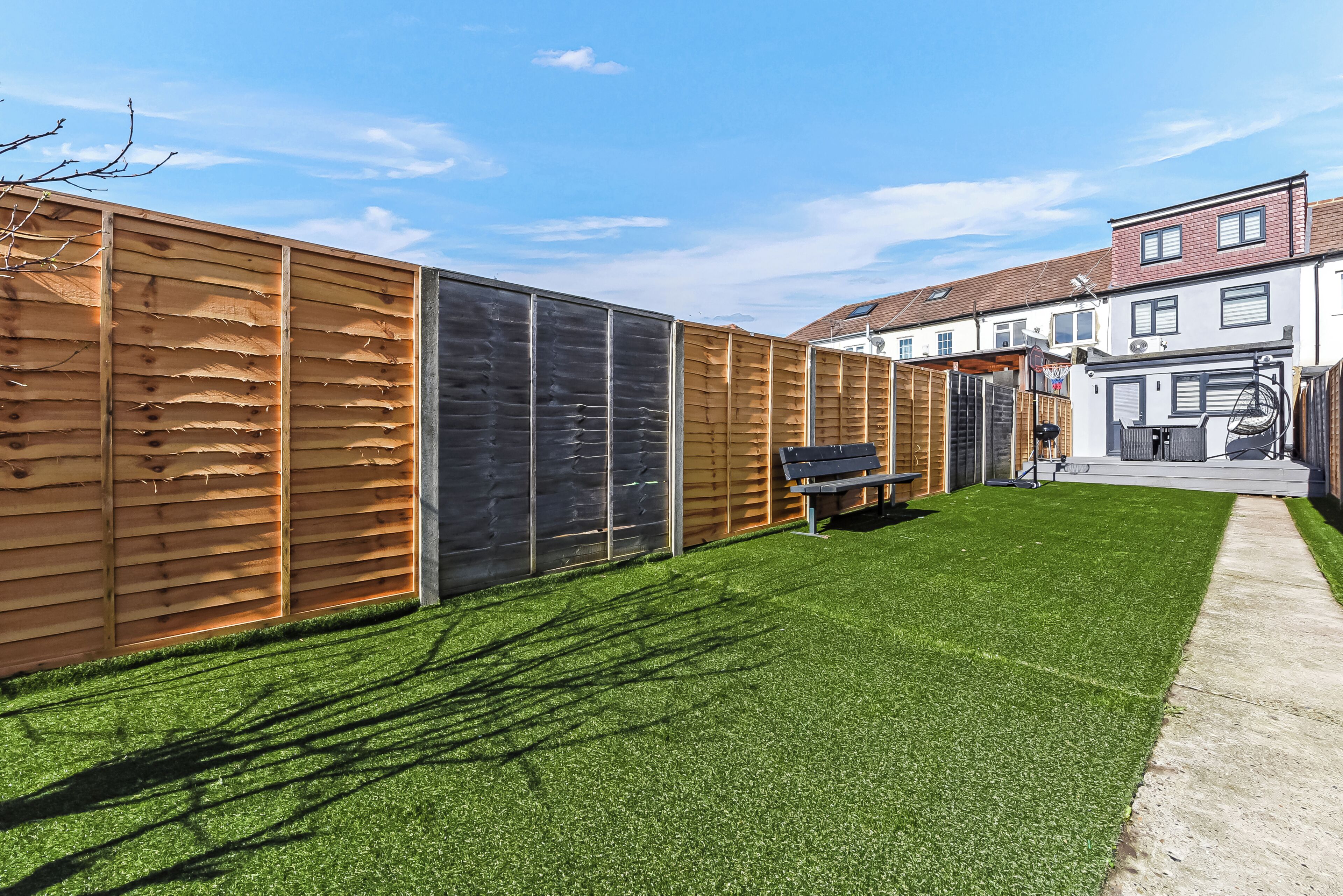 A backyard with artificial grass, a wooden fence, and a bench.
