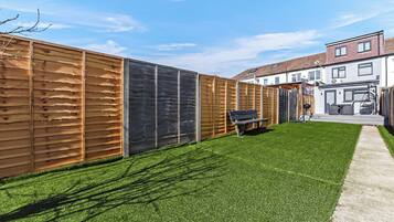 A backyard with artificial grass, a wooden fence, and a bench.