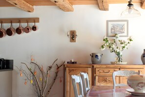Una cocina con ollas de cobre, una lámpara de pared, un florero con flores y un cuadro enmarcado.