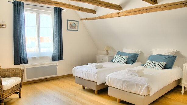 Un dormitorio con dos camas, una ventana con cortinas, piso de madera y un cuadro en la pared.