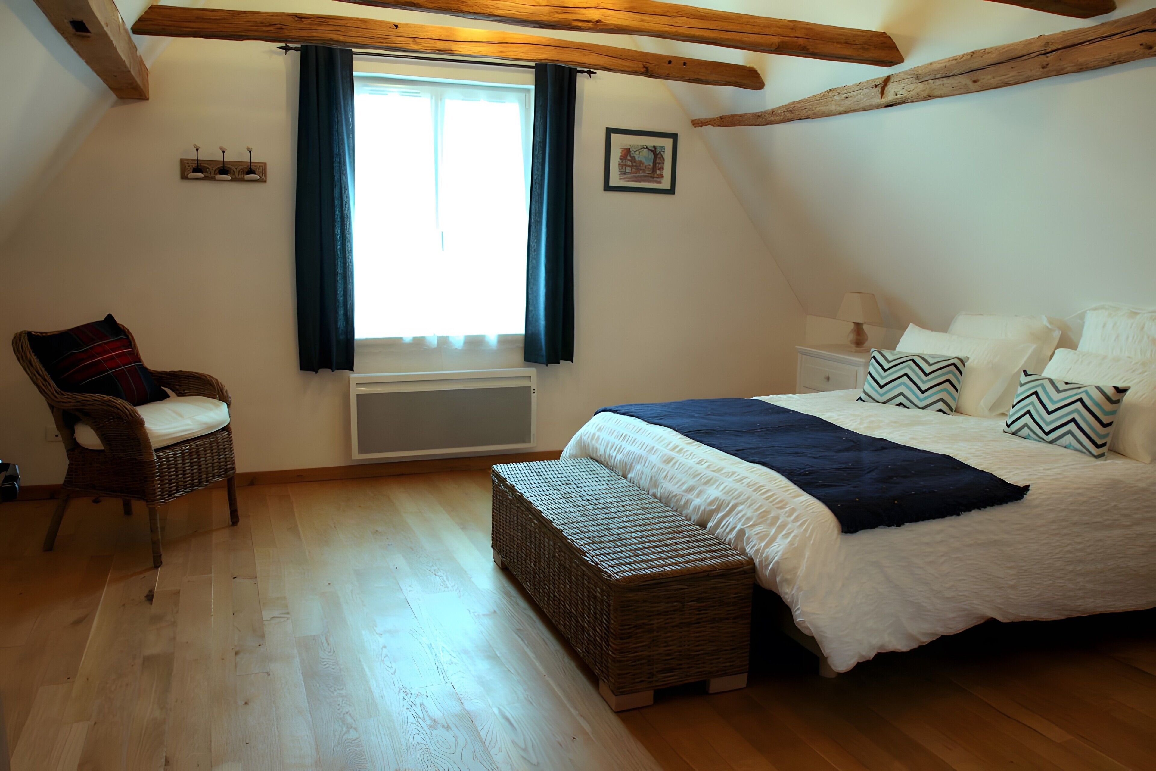 A bedroom with a bed, a chair, a bedside table, and a window with curtains.
