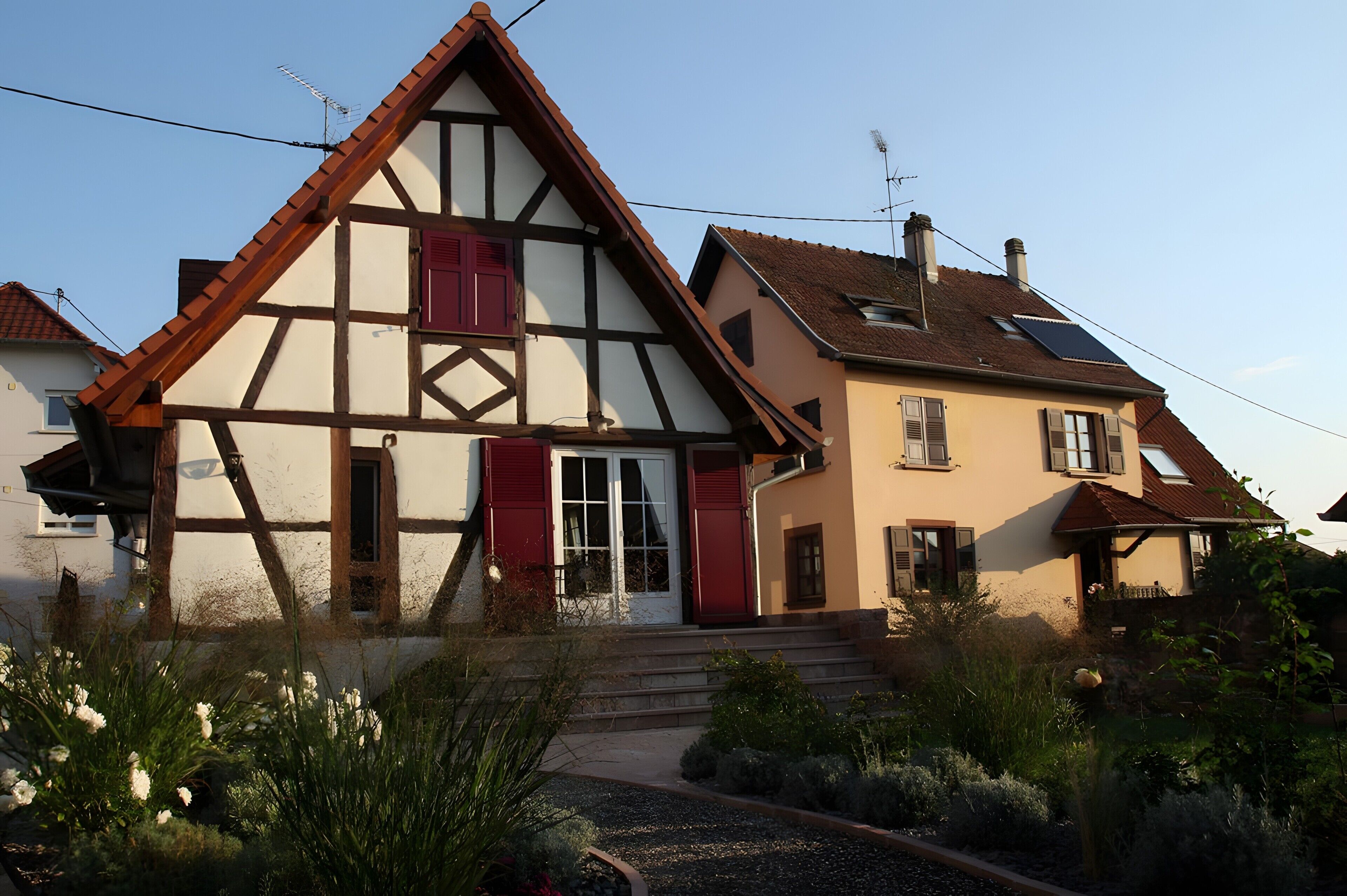 A traditional half-timbered house with a steep gable roof, red shutters, and a visible chimney.