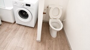 Pieni kylpyhuone, jossa on pesukone, wc ja pieni ikkuna.