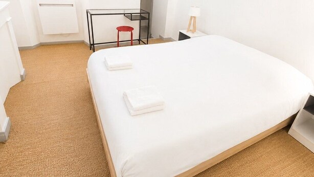 Hotellihuone, jossa on sänky, työpöytä, tuoli, lamppu ja ikkuna, jossa on verhot.