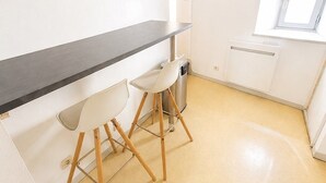 Pieni keittonurkkaus, jossa on musta työtaso, kaksi valkoista tuolia ja ikkuna, josta tulee luonnonvaloa.