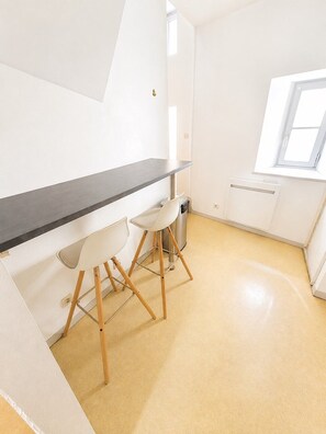 Eine kleine Küchenzeile mit schwarzer Arbeitsplatte, zwei weißen Stühlen und einem Fenster, das für natürliches Licht sorgt.