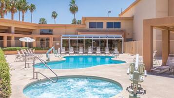 A pool area with multiple lounge chairs, a hot tub, and a covered seating area.