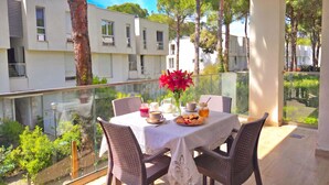 Un balcón con una mesa lista para comer, rodeado de sillas, con vistas a una zona residencial con árboles y edificios.