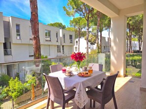 A balcony with a table set for dining, surrounded by chairs, overlooking a residential area with trees and buildings. - Beachside Apartment 308 (Gjiri Lalzit)