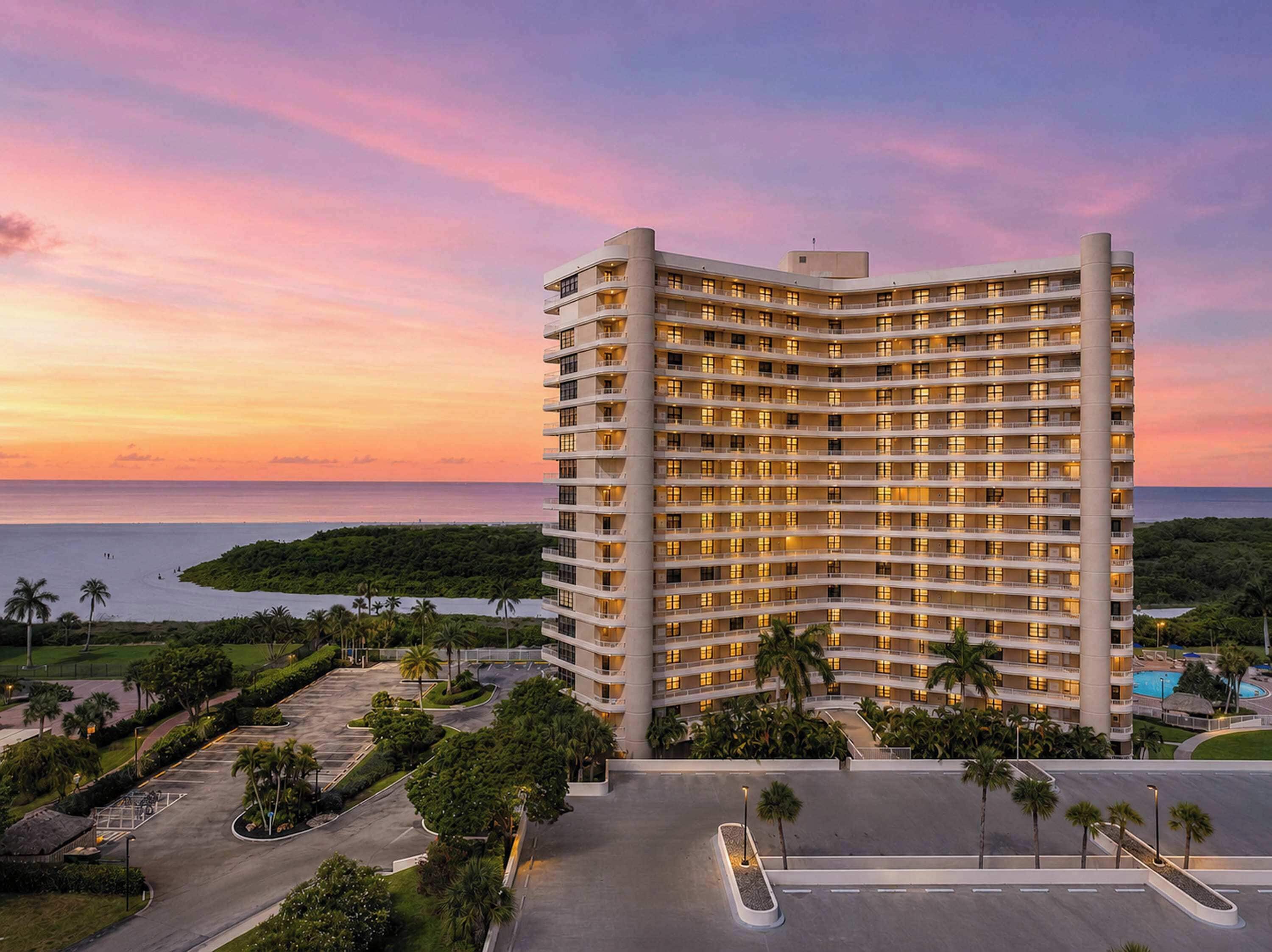 Un hôtel de grande hauteur doté de nombreux balcons, d’un parking et offrant une vue sur l’océan au coucher du soleil.