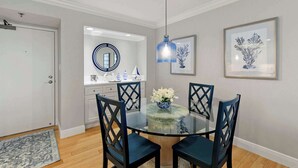 A dining area with a glass table, four chairs, a vase with flowers, a hanging light fixture, and framed artwork on the wall. - Remodeled Gulf-Front 2BR + Pool (Marco Island)