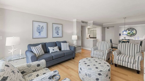 A living room with a sofa, armchairs, a coffee table, and a dining area with striped chairs. - Remodeled Gulf-Front 2BR + Pool (Marco Island)
