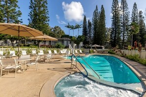 Una piscina con lettini e ombrelloni, circondata da alberi e un edificio.
