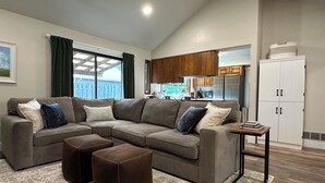 Ein Wohnzimmer mit Ecksofa, Poufs, einem kleinen Beistelltisch und Blick zur Küche.