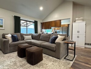 Una sala de estar con un sofá modular, otomanas, una mesita auxiliar y vista a la cocina.