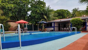 A swimming pool with a blue and red border, surrounded by lounge chairs and umbrellas. - Casa en Las Piedronas - piscina privada - AC - BBQ (Sonsonate Department)
