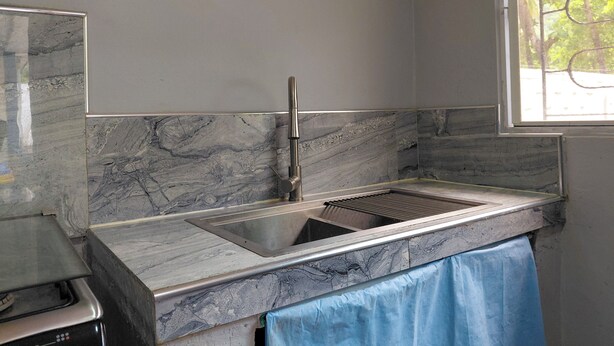 A kitchen with a marble backsplash, stainless steel sink, and a window with a view of trees. - Casa en Las Piedronas - piscina privada - AC - BBQ (Sonsonate Department)